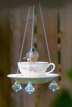 a bird sitting on top of a teacup hanging from a chain with crystal beads