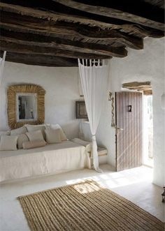 a white bed sitting under a wooden ceiling next to a doorway and window in a room