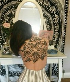 a woman sitting in front of a mirror with her back turned to the camera and tattoos on her body