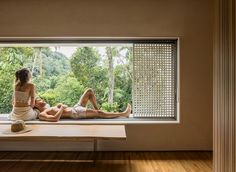 two people sitting on a window sill looking out at the trees and forest outside