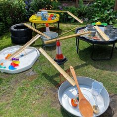 several buckets with paint and wooden spoons in them on the grass near flowers