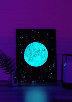 a blue full moon lit up in the night sky next to a plant and vase