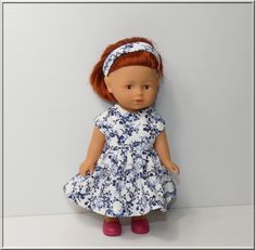 a doll with red hair wearing a blue and white dress, standing against a wall