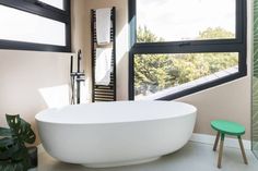 a large white bath tub sitting in a bathroom next to a green stool and window