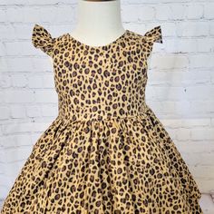 **Display dress is a size 3t on a size 3 mannequin and features a tulle petticoat underneath which is NOT INCLUDED in sale** This fun cheetah/leopard print dress features a boat neck, scoop back, optional flutter sleeves (as shown), and a full twirly skirt. There are matching fabric ties at the waist which tie into a bow in the back of dress.  The dress is made from 100% cotton and has a soft cotton liner. Kam snap closures in back make for easy on and off. (Kam snap colors will vary depending o Fitted Leopard Print Dresses With Ruffles, Cute Fitted Brown Dress, Summer Leopard Print Dresses With Ruffles, Summer Leopard Print Dress With Ruffles, Sleeveless Brown Tiger Print Dress, Brown Sleeveless Tiger Print Dress, One Wild Year, Baby Cheetah, Tulle Petticoat