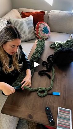 a woman sitting at a table working on some knitted items in her living room