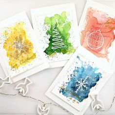 four cards with watercolor designs on them and one has a christmas ornament