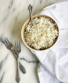 a bowl of rice and two forks on a marble counter top with a white towel