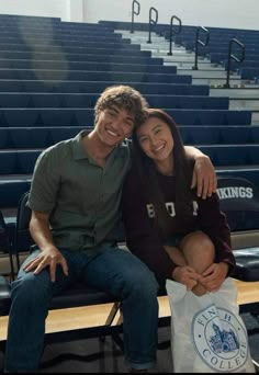 a man and woman sitting next to each other on a bench in front of bleachers