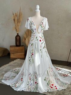 a white dress with red and green flowers is on display in front of a vase