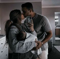 a man and woman are kissing while holding a baby in their arms as they take a selfie