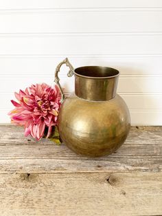 a metal vase sitting on top of a wooden table next to a pink flower bouquet