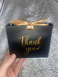 a person holding up a black box with gold foil writing on it that says thank you