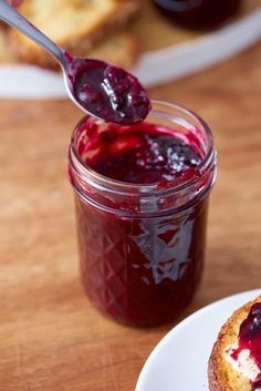 a spoon full of jam sitting on top of a white plate next to a muffin