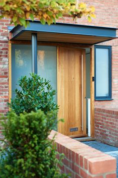 a wooden door sitting next to a green bush on top of a brick building in front of a window