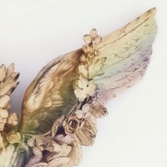 a bird statue with wings and flowers on it's back end, against a white background