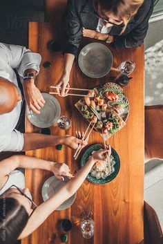 three people sitting at a table with plates and bowls on it, one person is serving food to the other