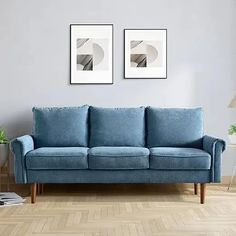 two framed pictures hang on the wall above a blue couch in a room with hardwood floors