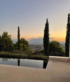 an outdoor swimming pool surrounded by trees and bushes at sunset with the sun setting in the distance