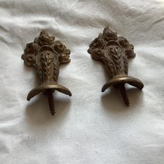 two antique brass sconces are on a white sheet, one has a bird's head and the other is an elephant's tail