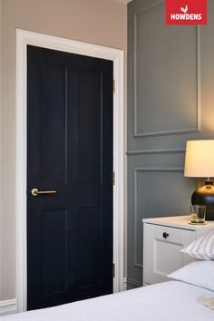 a black door in a bedroom next to a white bed and nightstand with a lamp on it