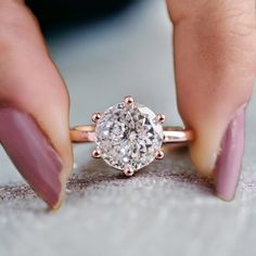 a woman's hand with pink nails and a ring on her finger, holding a diamond