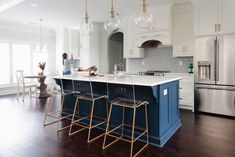 a kitchen with white cabinets, blue island and gold bar stools in the center