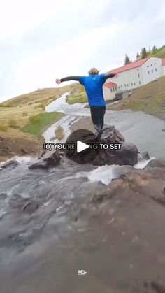 a man standing on top of a rock in the middle of a river with his arms outstretched