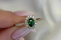 a woman's hand holding an emerald and diamond ring