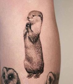 an animal tattoo on the thigh with three otters and one is holding something in it's mouth