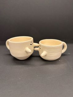 two white cups with faces on them sitting next to each other in front of a gray background