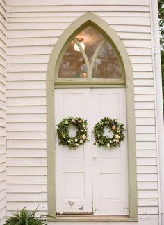 two wreaths are placed on the front door of a white church with green trim