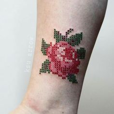 a cross stitch rose tattoo on the right leg, with green leaves and red flowers