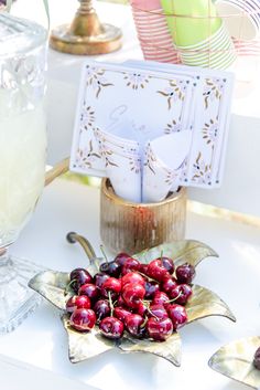 cherries are sitting on a plate next to a vase with flowers and cards in it