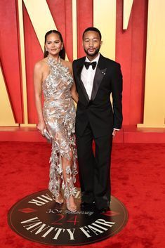 a man and woman in formal wear standing on a red carpet with the word vanity written on it