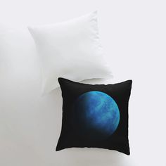 a black pillow with a blue planet on it next to a white pillow cover and two pillows