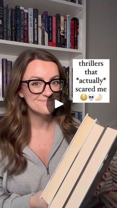 a woman holding a stack of books in front of a book shelf with an ad on it