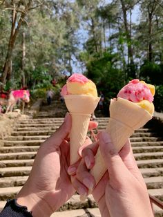 two people holding up ice cream cones in front of some steps and trees on the other side