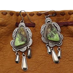 Traditional Navaho silver earrings featuring a single setting of gaspeite handcrafted by silversmith Shiela Tso. These earrings feature stamp work appliqué and reppousse work by a talented artist. Earrings have a hanging length of 2 1/2" and are 7/8" wide at their widest point. Weight for both earrings is approximately 17.4 grams. Unique Charms, Timeless Beauty, Statement Pieces, The Beauty, Native American, Silver Earrings, Stamp, Silver, Beauty