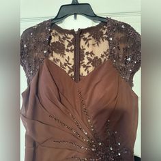 the back of a brown dress with sequins and beads on it, hanging from a hanger