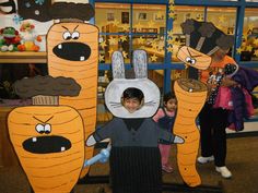 two children are standing in front of cardboard carrots that look like they have faces on them