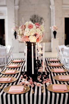 a black and white striped table cloth with pink napkins, gold plates and candles