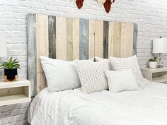 a bed with white sheets and pillows in a room next to a brick wall that has wood planks on the headboard