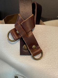 a white purse with a brown leather strap and metal ring on the front, sitting on a table