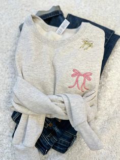 Our sweet little ribbon bow sweatshirt is not only on trend this season but completely adorable!   Cute and cozy for any girly girl you know or for yourself!  So go ahead, throw a ribbon around your ponytail and pair this cutie with your favorite jeans or leggings! Shown here in oatmeal with rose thread! Features: 8 oz., 50% USA cotton, 50% polyester Pill-resistant air jet yarn Made with 50% sustainably and fairly grown USA cotton Feature: Pill-resistant air jet yarn These are unisex sizing, fit Cute Embroidered Sweatshirt Gift, Cute Custom Embroidery Sweatshirt For Winter, Cute Winter Sweatshirt With Custom Embroidery, Clothes With Bows, Embroidery Sweatshirt Ideas, Bow Clothing, Bow Sweatshirt, Monogram Bow, Greenville Nc