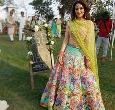 a woman in a floral print lehenga and yellow shawl is posing for the camera