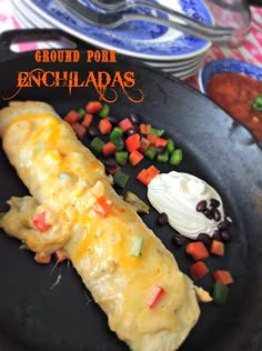 an enchiladas is on a black plate with vegetables and sour cream in the background