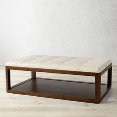 a wooden coffee table with a white leather cushion on it's top and bottom shelf