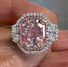 a pink diamond surrounded by two white diamonds in a halo setting with an oval center stone