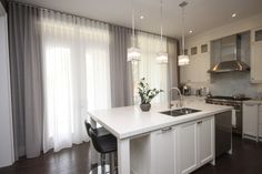 a kitchen with white cabinets and an island in front of a window that has sheer curtains